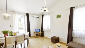 A living room with a television, a dining area with chairs and a table, a sofa, and a small table with a decorative item. - Bright flat with shared pool in Tar (Tar)