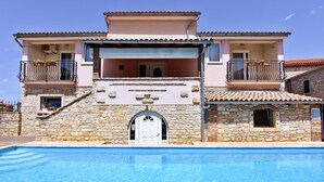 A two-story building with a stone facade, a swimming pool in front, and balconies with railings. - Bright flat with shared pool in Tar (Tar)