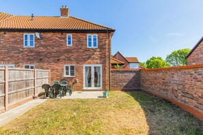A two-story brick house with a tiled roof, a fenced backyard, and a patio with outdoor furniture. - A slow Norfolk weekend in a village near Norwich (Norwich)