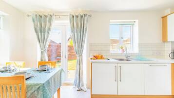 Une cuisine moderne avec des meubles blancs, une fenêtre et un coin repas avec une table mise pour deux personnes.
