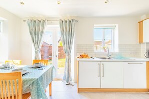 A modern kitchen with white cabinets, a window, and a dining area with a table set for two. - A slow Norfolk weekend in a village near Norwich (Norwich)