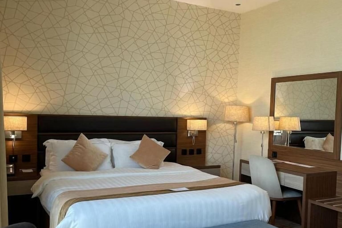 A hotel room with a large bed, bedside tables with lamps, a desk, a chair, and a mirror.
