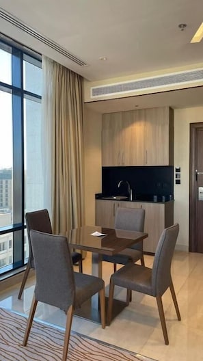 A modern dining area with a table and chairs, a kitchen in the background, and a large window with curtains. - RIO OLAYA HOTEL  (Riyadh)