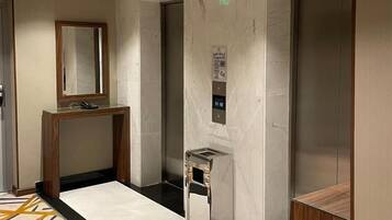 Een moderne lift met een digitaal scherm, een marmeren wand en een houten console tafel.