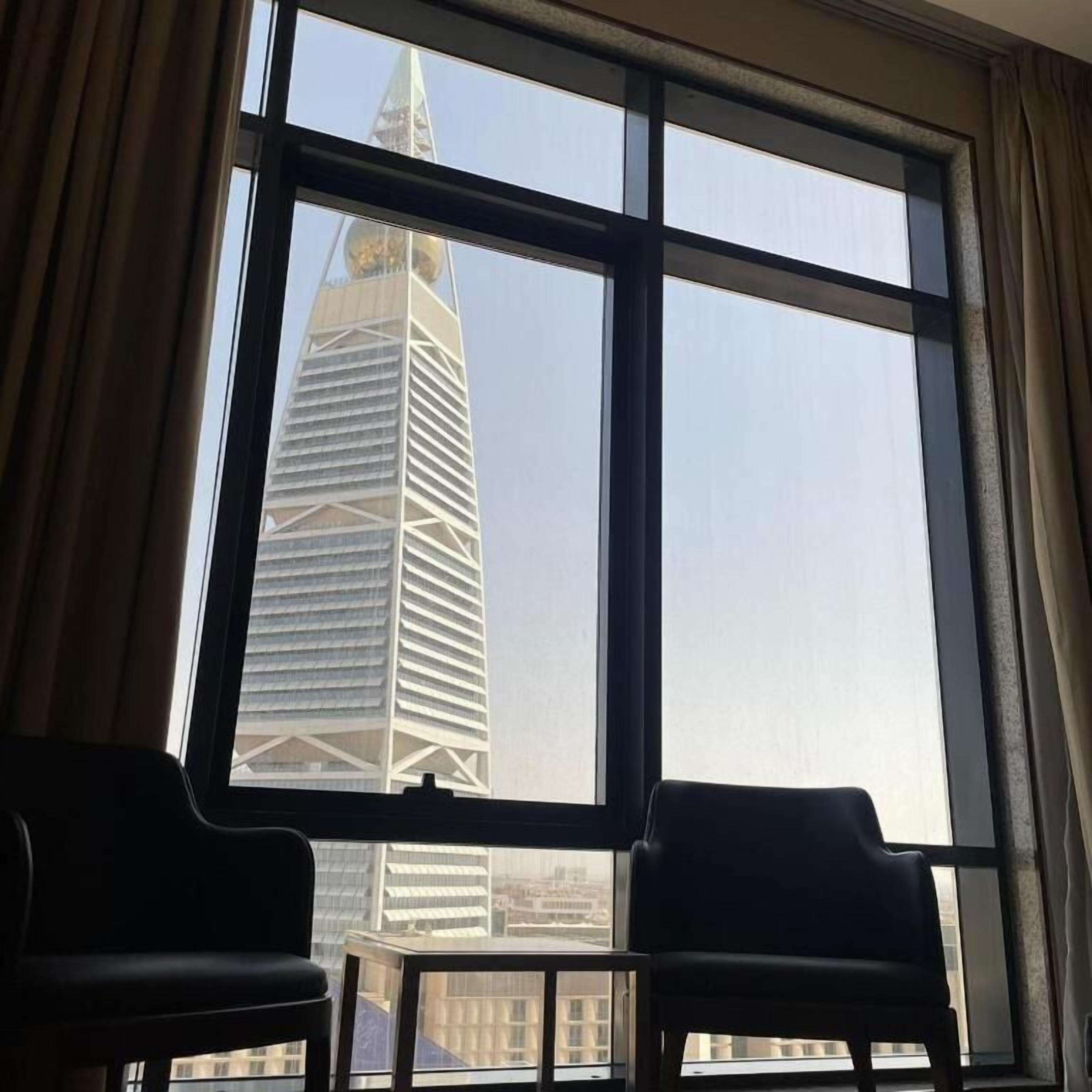 A room with a large window, two chairs, and a view of a tall building.