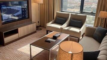 Een moderne hotelkamer met een grote televisie, twee banken, een salontafel en uitzicht op de stad.