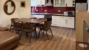 A modern kitchen with white cabinets, a red backsplash, and a dining area with a wooden table and chairs. - Hotel La Cita (Tirana)