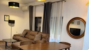 A modern living room with a sofa, a wooden dining table with chairs, a round mirror, and pendant lighting. - Hotel La Cita (Tirana)