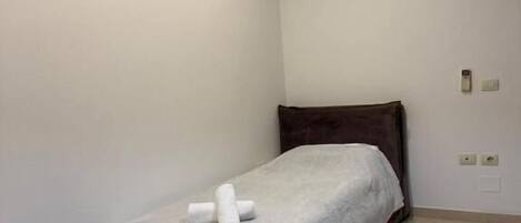 A small, neatly arranged bedroom with a bed, bedside table, and an air conditioning unit.