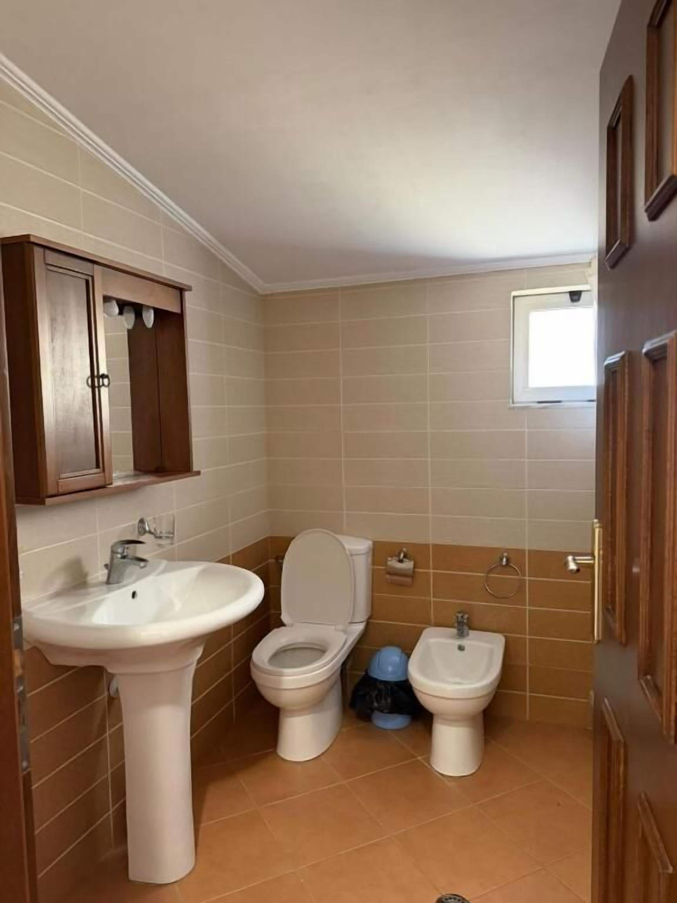 Une salle de bain équipée d’un lavabo, de toilettes, d’un bidet et de meubles en bois.