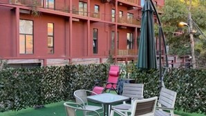 A multi-story building with balconies, a patio area with chairs and a table, and a green hedge. - Hotel La Cita (Tirana)