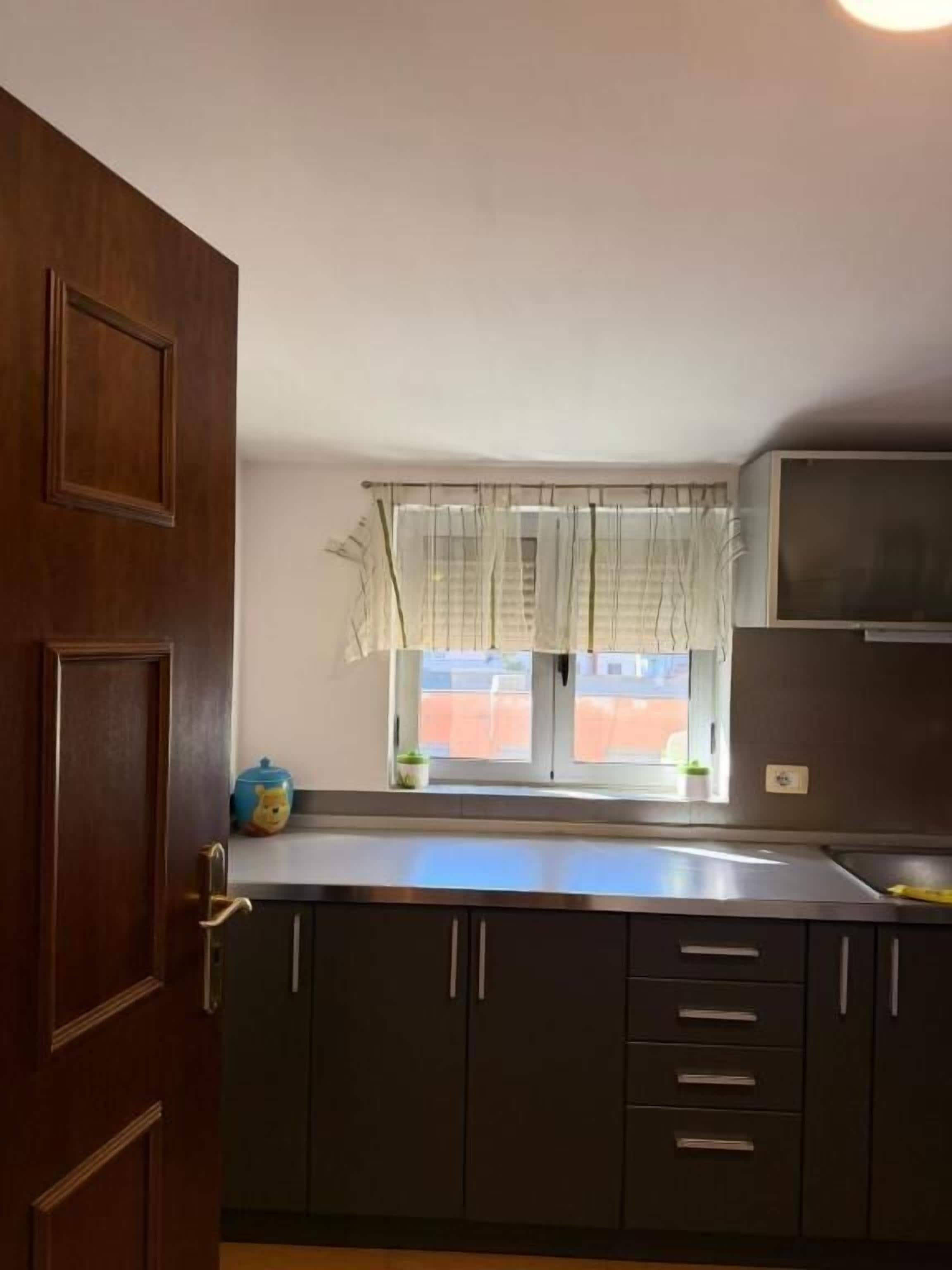 Una cucina con mobili scuri, una finestra con tende leggere e una piccola pianta sul davanzale.