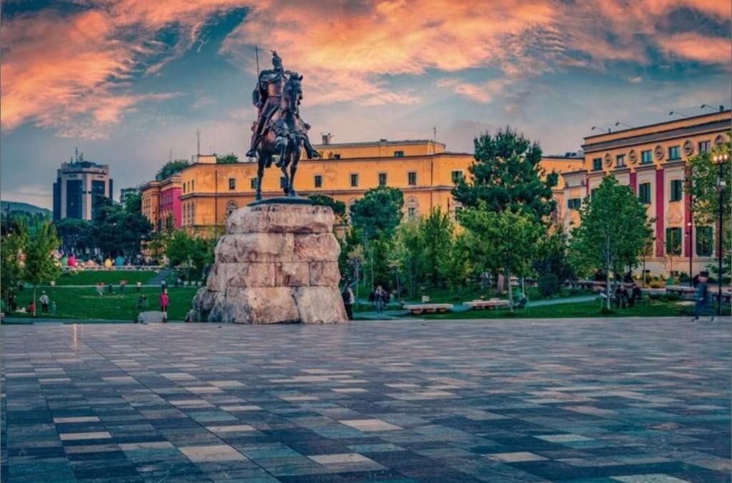 Uma estátua numa praça pública, com edifícios ao fundo.