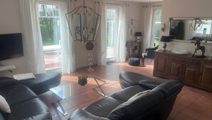 A living room with a glass coffee table, leather sofas, a TV, and a bookshelf.