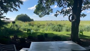 A table with chairs under a tree, a grassy field, and wind turbines in the distance.