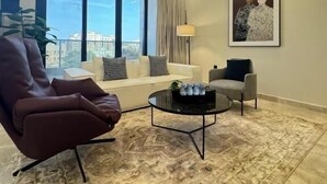 A modern living room with a sofa, armchairs, a coffee table, and a large window offering a city view. - Khozama Living (Jeddah)