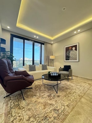 A modern living room with a sofa, armchairs, a coffee table, and a large window offering a city view. - Khozama Living (Jeddah)