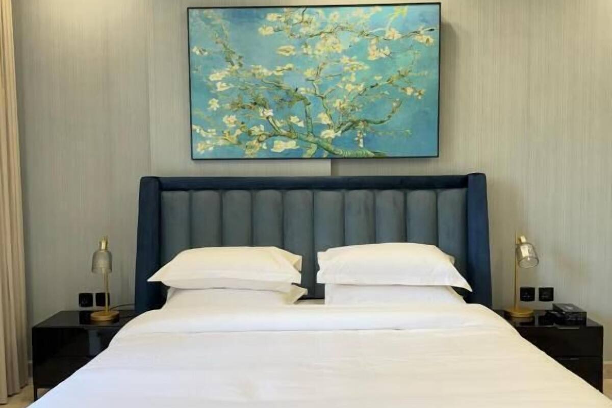 A neatly made bed with a headboard, two bedside tables with lamps, and a large painting on the wall.