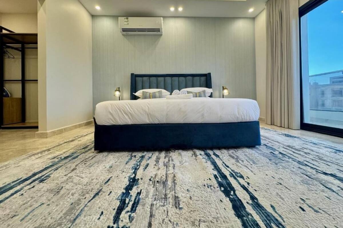 A modern bedroom with a large bed, a ceiling air conditioner, and a large window.