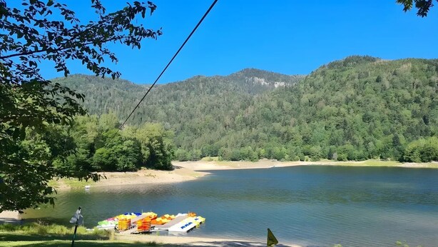 A lakeside view with a wooden dock, boats, and a forested hill in the background. - La Maison du Portier: Mountain View, Private Terrace with Fire Pit and Wi-Fi (Malmerspach)
