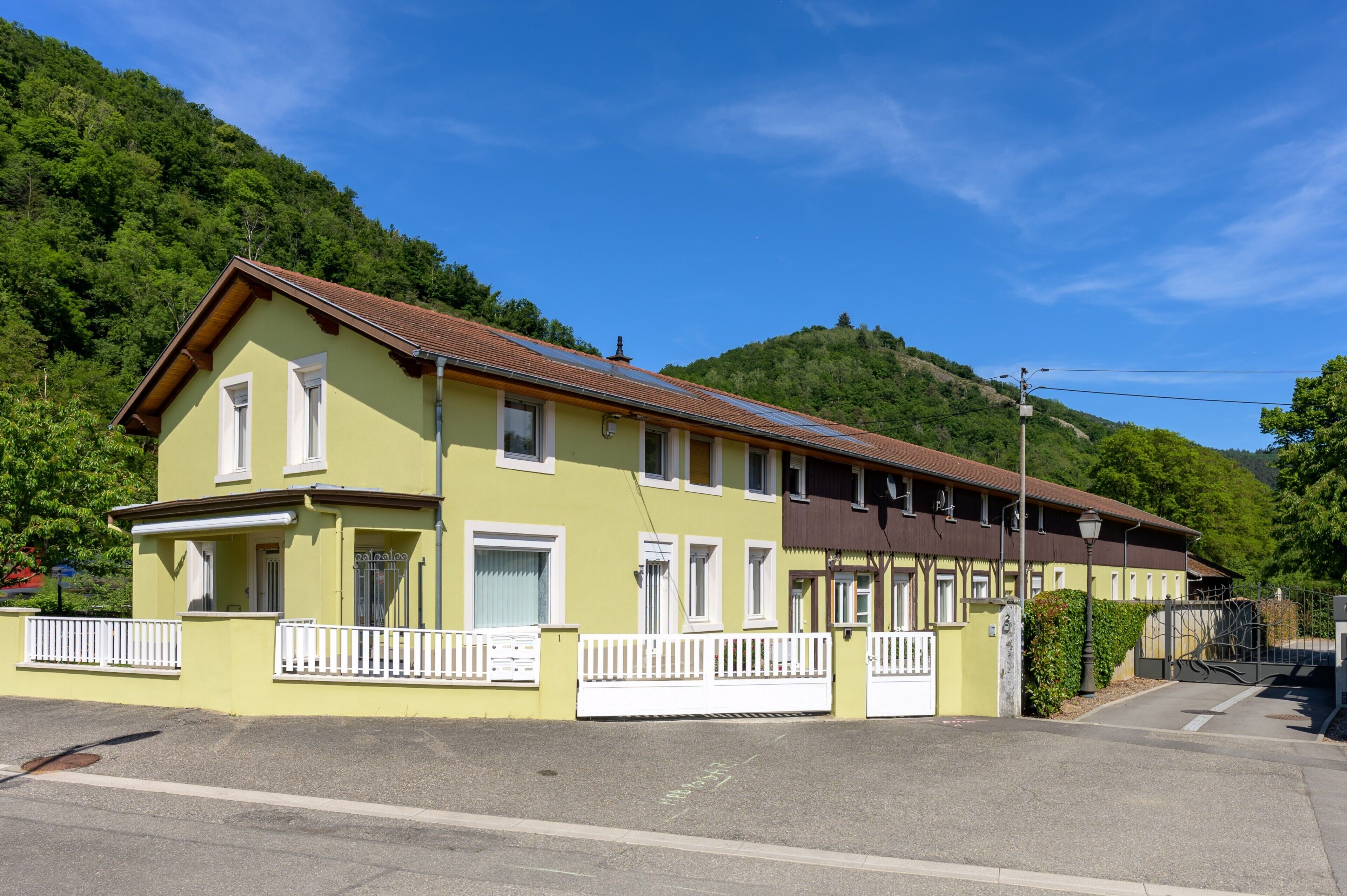 Um edifício de dois andares com fachada amarela, grades brancas e telhado castanho.