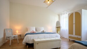 A bedroom with a bed, a bench, a chair, a wardrobe, and a small table with a lamp. - La Maison du Portier: Mountain View, Private Terrace with Fire Pit and Wi-Fi (Malmerspach)