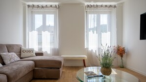 A living room with a sectional sofa, a glass coffee table, a bench, and two windows with sheer curtains. - La Maison du Portier: Mountain View, Private Terrace with Fire Pit and Wi-Fi (Malmerspach)