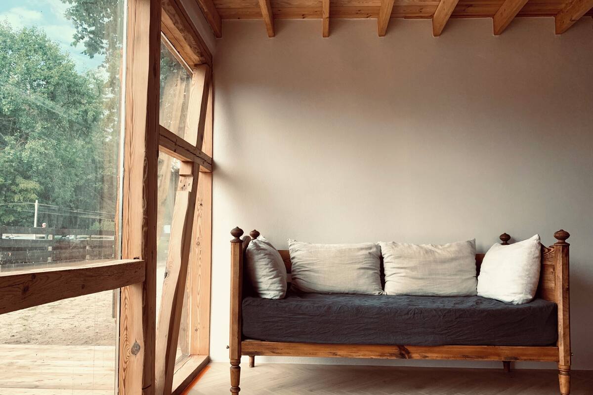 Una ventana con marco de madera, suelo de madera y un sofá de madera con cojines.