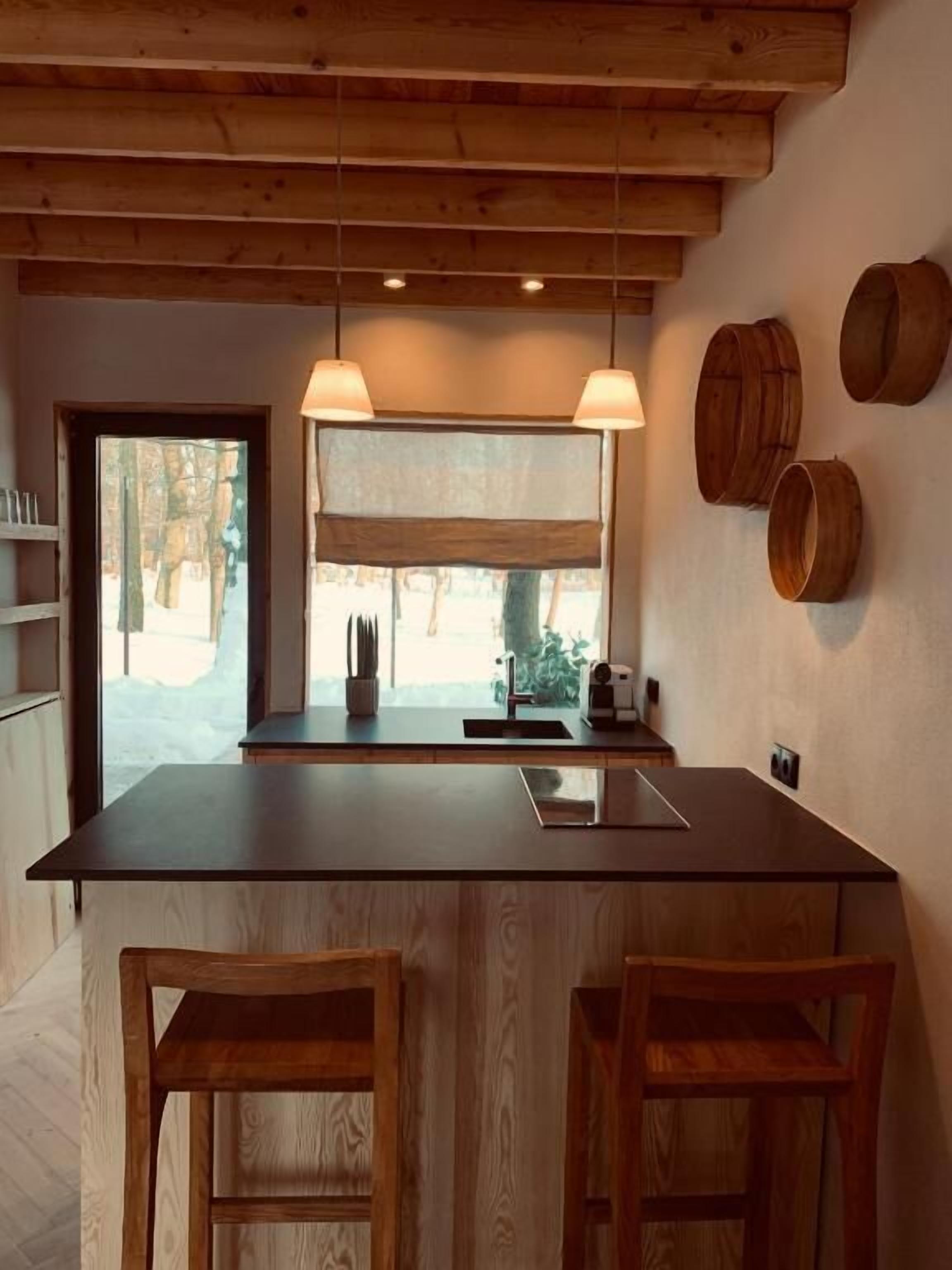 A kitchen with a large island, wooden bar stools, pendant lights, and a view of the outdoors.
