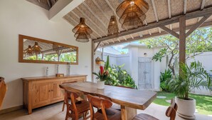 A wooden dining table with chairs, a wooden cabinet, wicker pendant lights, and a large mirror. - New Villa Misha Modern 2BR Pool with Tropical Garden Near Seminyak (Badung)