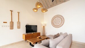A modern living room with a wooden coffee table, a beige sofa, a TV, and wall-mounted decor. - New Villa Misha Modern 2BR Pool with Tropical Garden Near Seminyak (Badung)