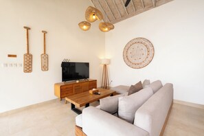 A modern living room with a wooden coffee table, a beige sofa, a TV, and wall-mounted decor. - New Villa Misha Modern 2BR Pool with Tropical Garden Near Seminyak (Badung)