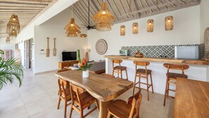 A spacious kitchen with wooden countertops, a dining area with a large wooden table and chairs, and a ceiling with exposed beams and hanging wicker lights. - New Villa Misha Modern 2BR Pool with Tropical Garden Near Seminyak (Badung)