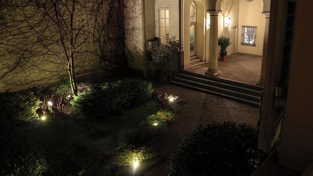 An outdoor courtyard with a stone wall, a tree, and a pathway leading to a building entrance. - Elegant apartment in the center of Turin. (Torino)