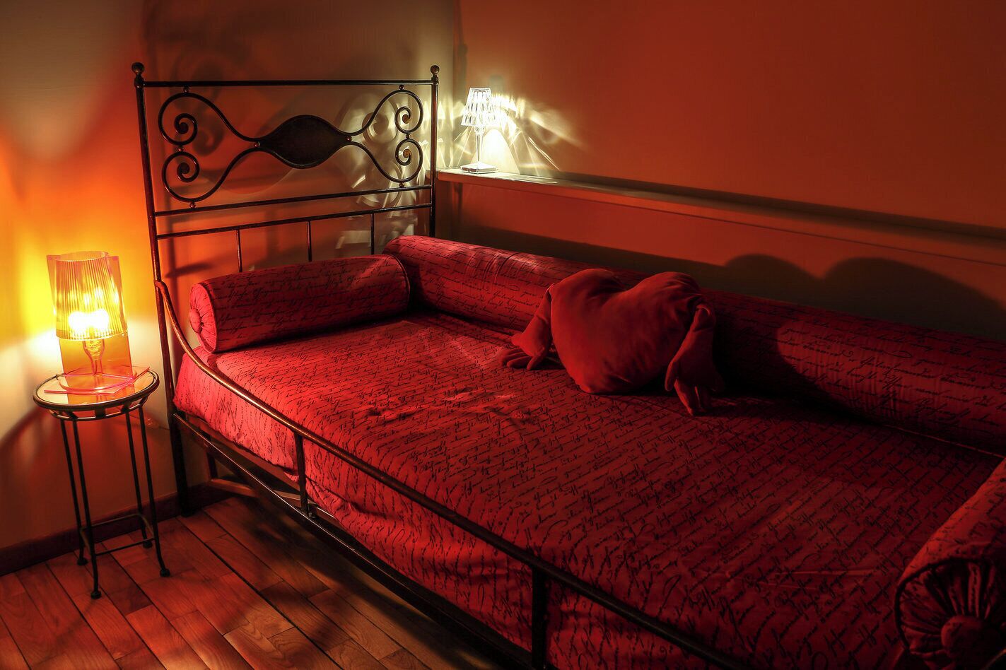 Een eenpersoonsbed met metalen frame, een nachtkastje met lamp en een wandlamp.