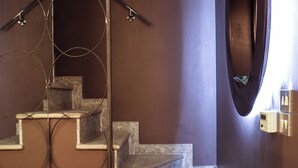 A staircase with a circular mirror and a wall-mounted light fixture. - Elegant apartment in the center of Turin. (Torino)