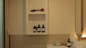 Un baño con un lavabo blanco, un espejo y tres botellas de líquido en una repisa.