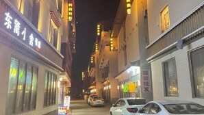 Una calle estrecha flanqueada por edificios, algunos con letreros iluminados.