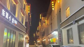 A narrow street with buildings on either side, some with illuminated signs, and parked cars.
