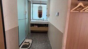 Un pasillo estrecho que conduce a un baño con espejo, lavamanos y un perchero de madera.