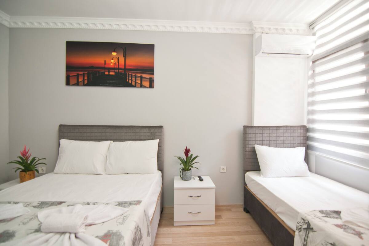 A bedroom with a bed, a nightstand, a potted plant, and a painting on the wall.