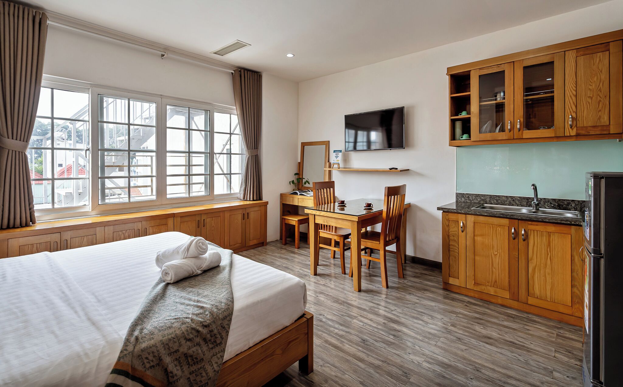 Ett hotellrum med en säng, ett skrivbord med en stol, en tv, träskåp och ett fönster med gardiner.