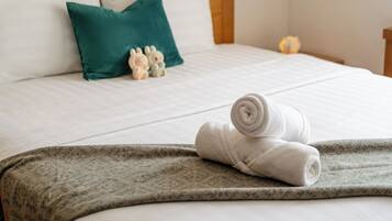 Una cama bien hecha con una toalla blanca enrollada, un cojín verde y una pequeña figurita.