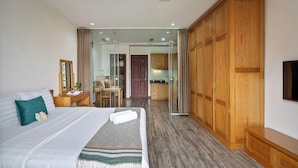 Ein Hotelzimmer mit Bett, Schreibtisch, Stuhl, Kleiderschrank, Fernseher und einer Glastür zu einem Badezimmer und einer Küchenzeile.