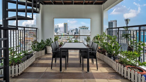 Ein Balkon mit Tisch und Stühlen, umgeben von Kübelpflanzen, mit Blick auf eine Stadtlandschaft.