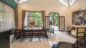 Una habitación amplia con techo alto, un comedor con mesa y sillas, un sofá y un ventanal con cortinas.