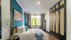Un dormitorio con cama, mesita de noche, un jarrón con ramas, un cuadro en la pared y una ventana con cortinas.