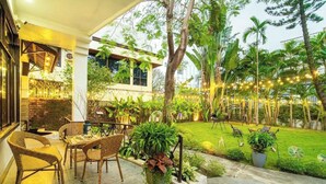 Un patio al aire libre con mobiliario de mimbre, plantas en macetas y guirnaldas de luces.