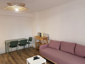 Una habitación con una mesa de comedor de madera, dos sillas, un sofá, una pequeña mesita de madera con un tostador y una lámpara colgante.