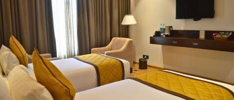 A hotel room with two beds, a chair, a desk with a flat-screen TV, and a window with curtains.